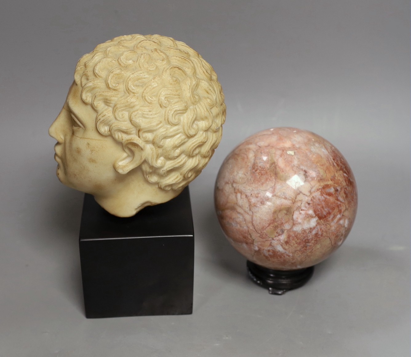 A simulated marble Roman head ornament, 24 cm and a rouge marble ball on stand, 15 cm